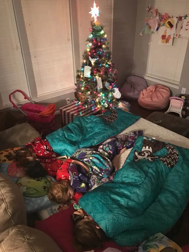 Three children sleeping in sleeping bags beside a Christmas tree