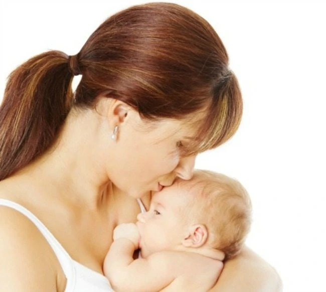 Mother kissing newborn baby holding in hand over white background