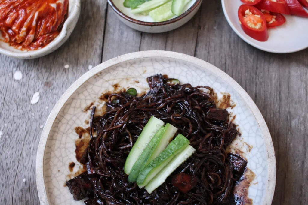 a white ceramic dish with a pile of black bean noodles on it and a few strips of cucumber as a garnish. Black bean noodles are a great pasta alternative.