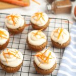 Grain-free carrot cake cupcakes with cream cheese frosting and carrot zest garnish on a cooling rack.