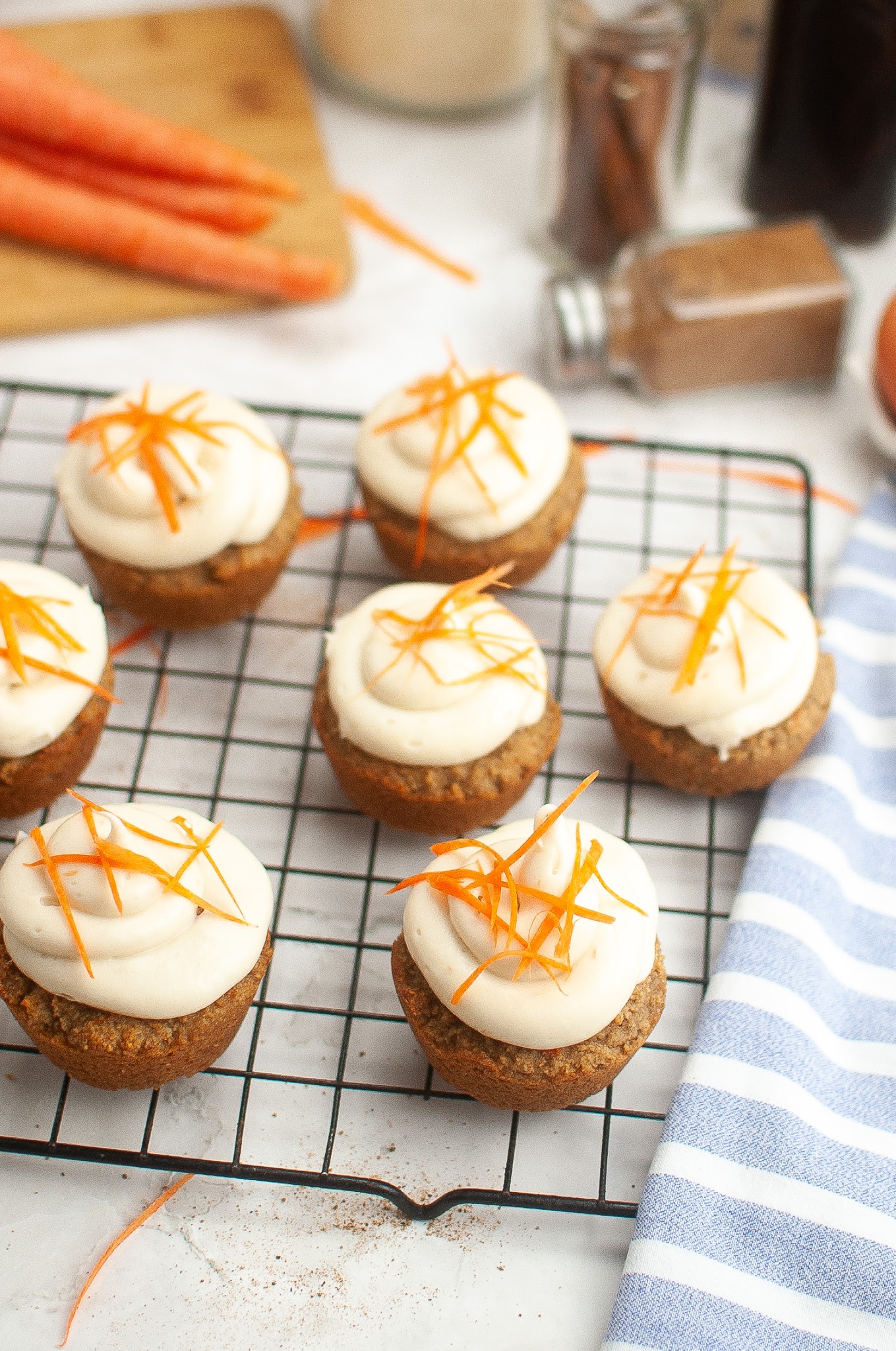 Grain-free carrot cake cupcakes with cream cheese frosting and carrot zest garnish on a cooling rack.