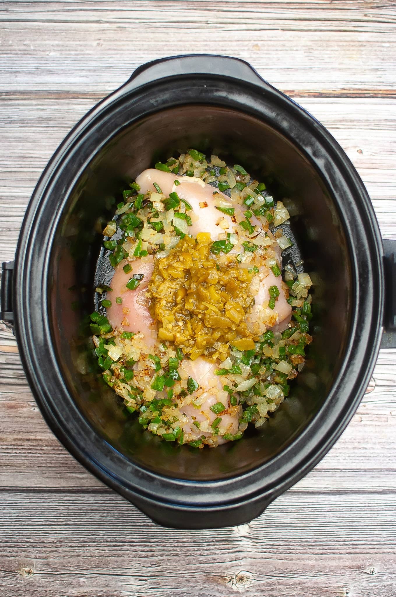 A crock pot filled with chicken and herbs to make white chicken chili.