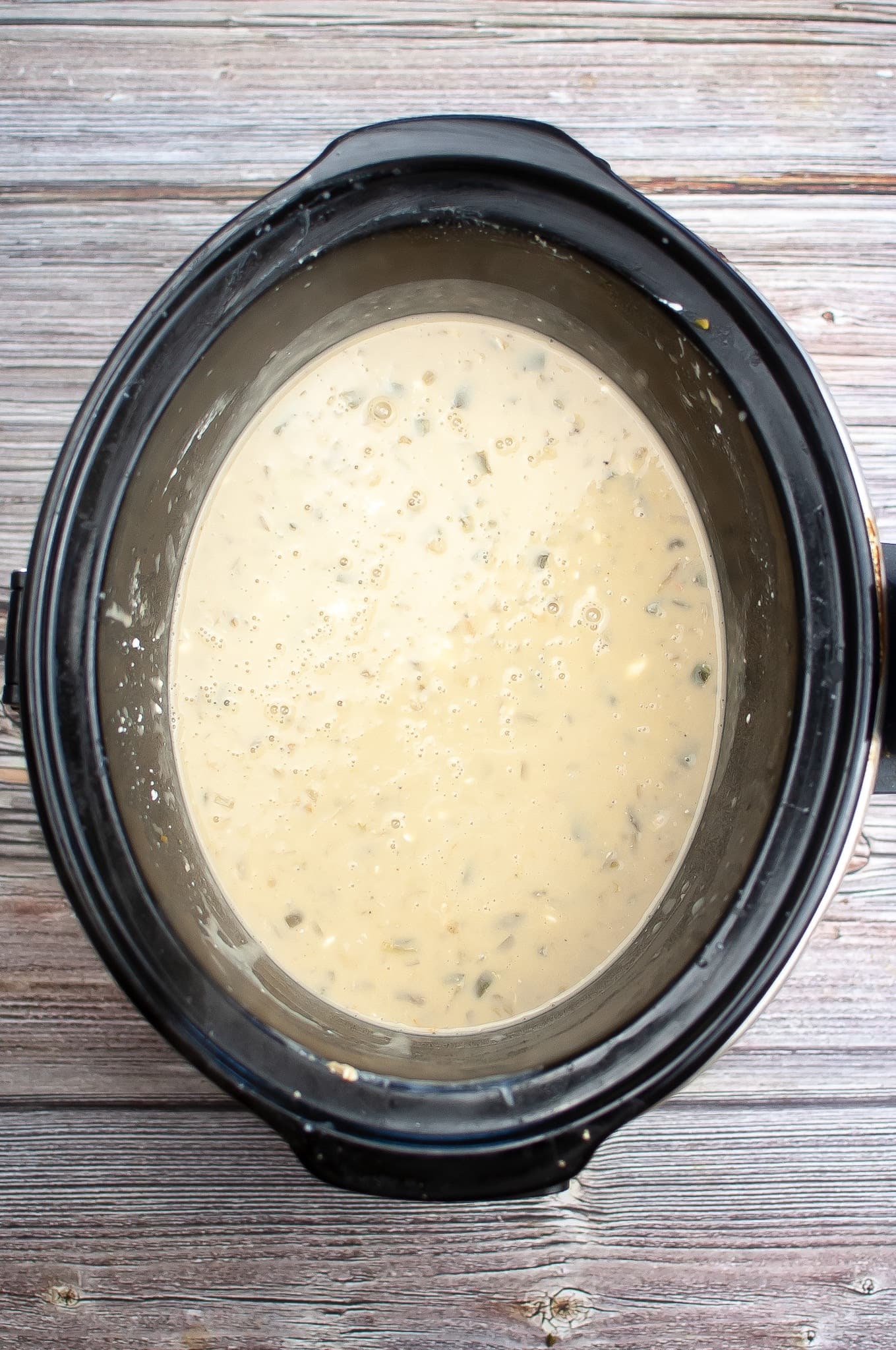 A crock pot with a white liquid inside to make slow cooker white chicken chili.