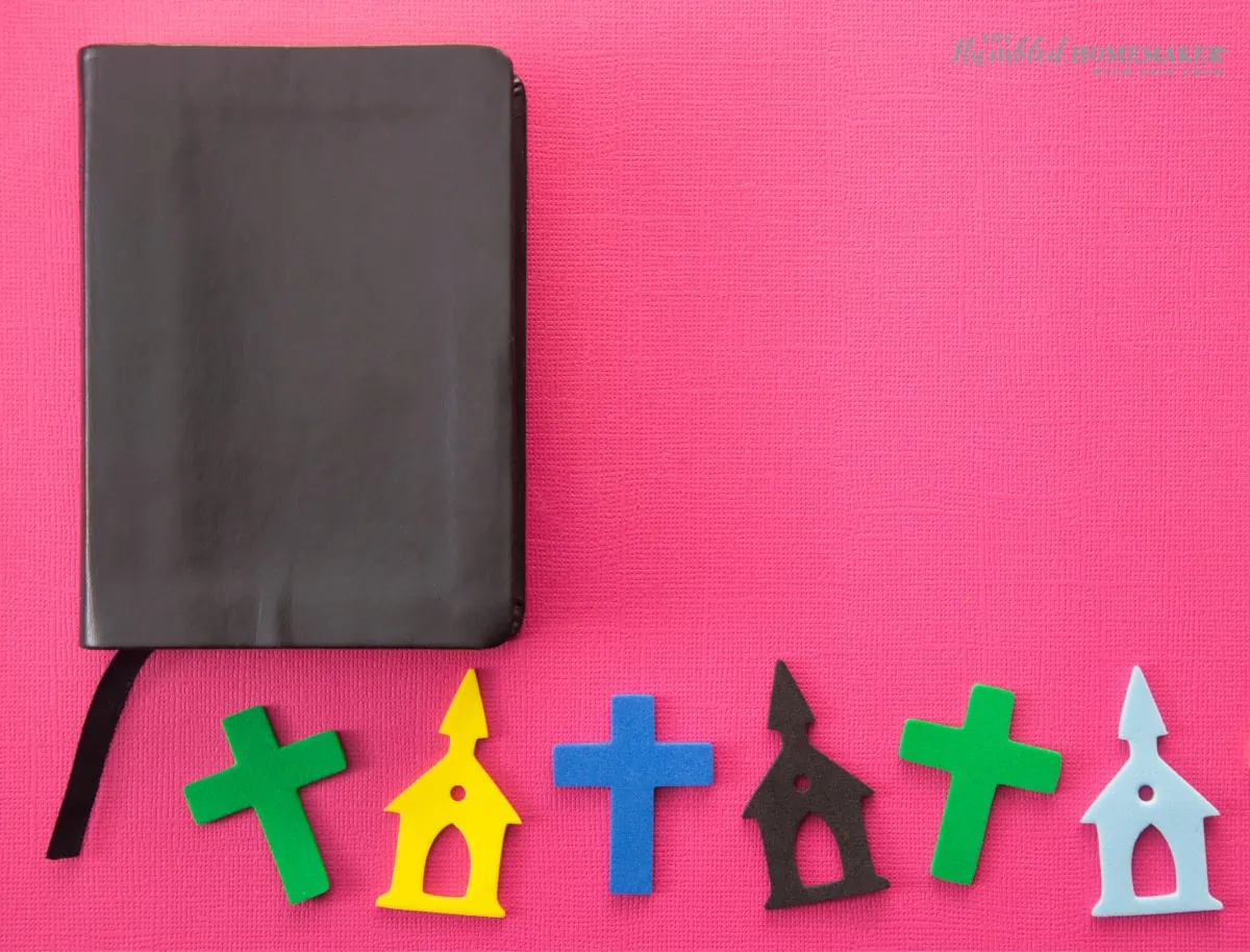 A black notebook with a ribbon bookmark next to colorful cut-out shapes of religious symbols representing resurrection on a pink background.