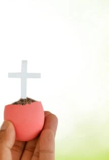A hand holding a cross in an Easter basket.