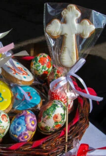 A basket of Easter cookies and eggs including a cross cookie and the Greek symbol for Christ is Risen painted on cookies.