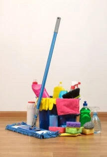 Assorted cleaning supplies and equipment arranged on a wooden floor against a wall.