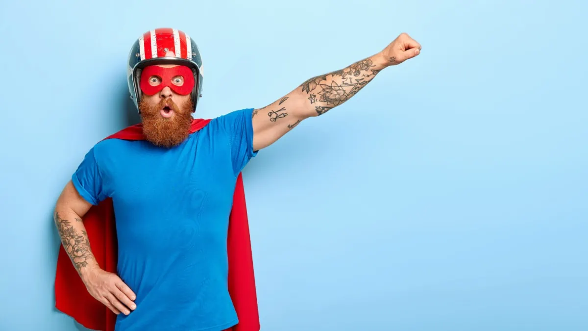 A bearded man wearing a superhero mask and cape, showcasing subscription boxes for men on a blue background.