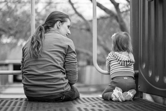 Mother and child sitting together at the playground. Getting down at eye level is just one ways to help time stand still and promote moments of connection with your kids.
