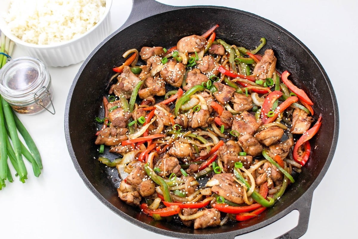 Chicken stir fry in a skillet with peppers and rice.