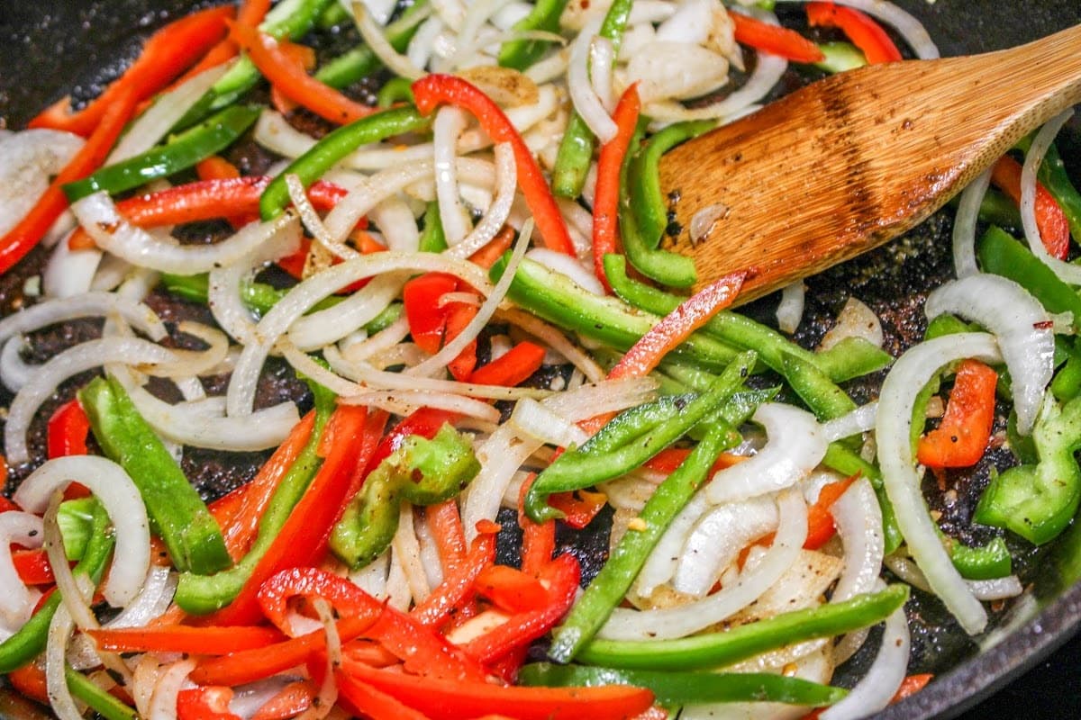 Onions and peppers in a pan with a wooden spoon.