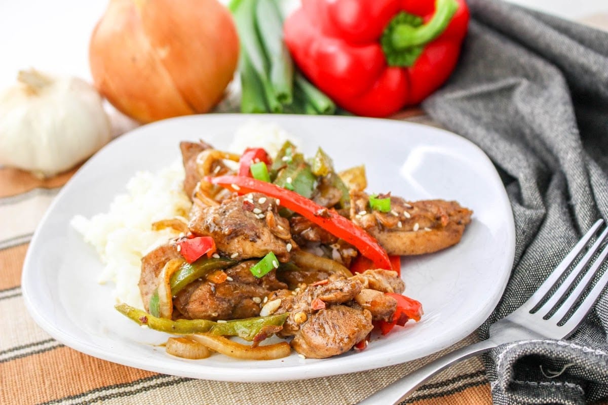 A plate of stir fried chicken with peppers and onions.