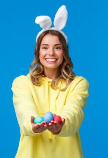 A young woman wearing bunny ears and holding Easter eggs on a blue background.