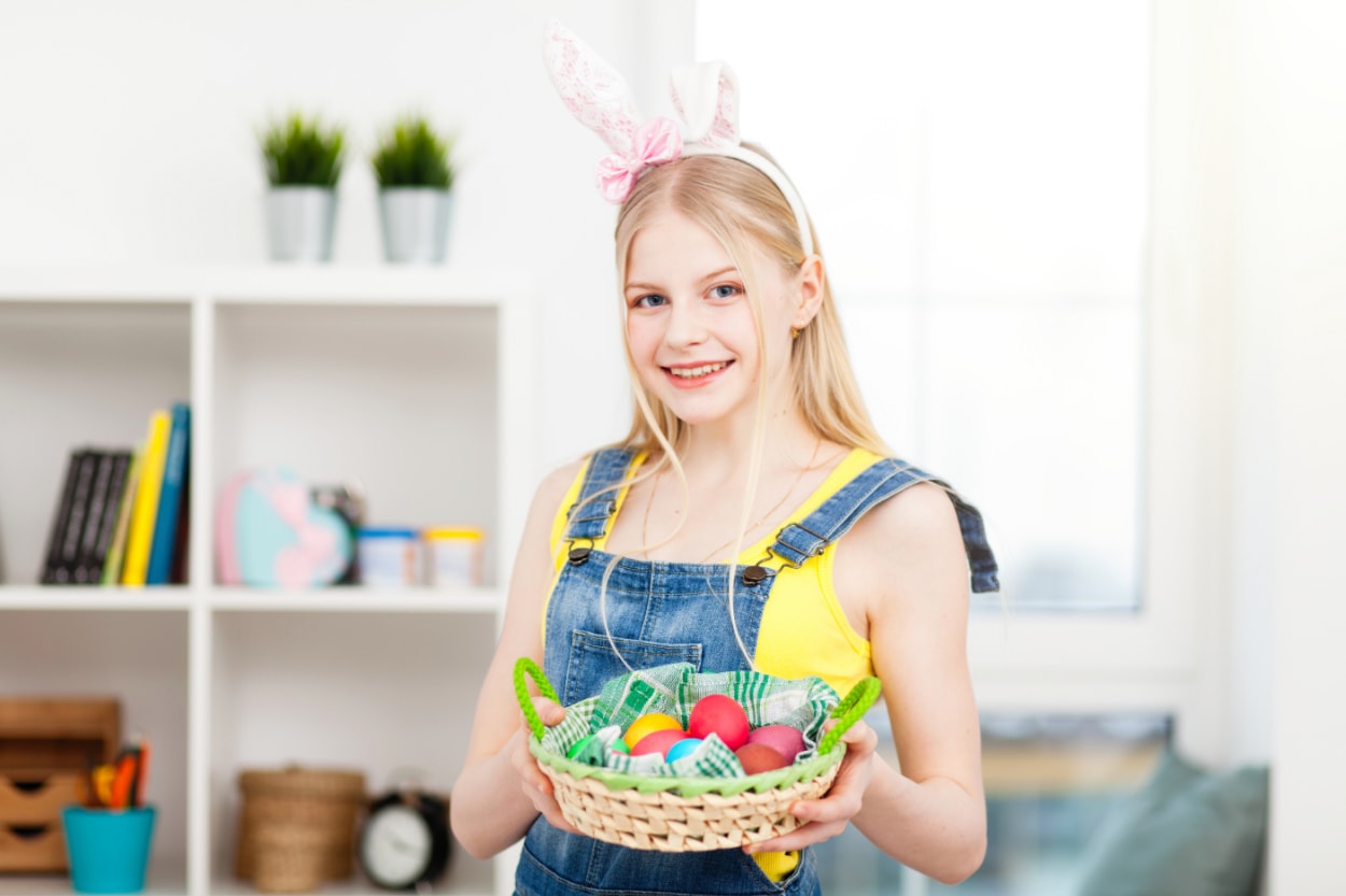 A teenage girl with bunny ears holding a basket of easter eggs.