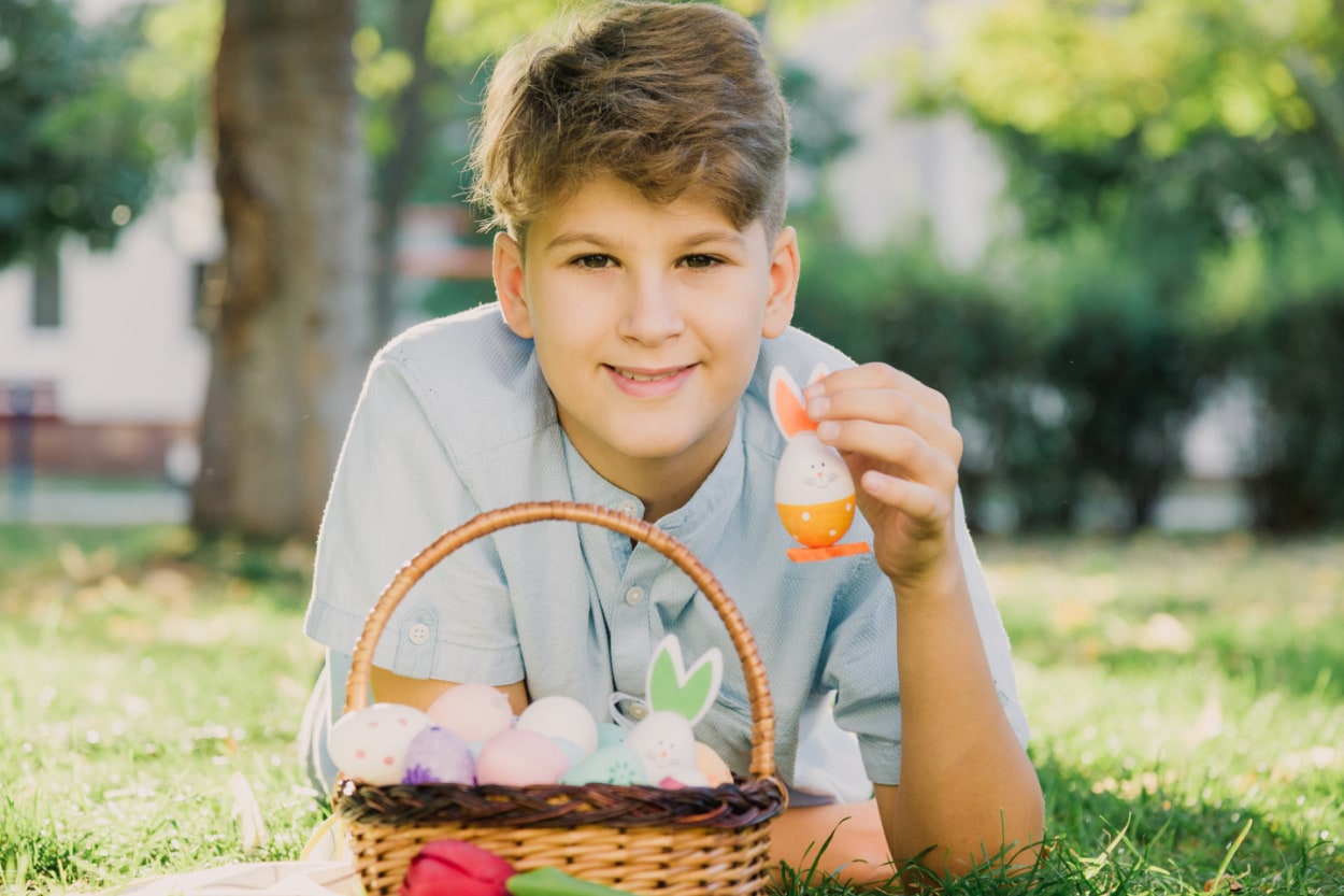A young boy laying on the grass with a basket of easter eggs. Easter basket ideas for teenagers