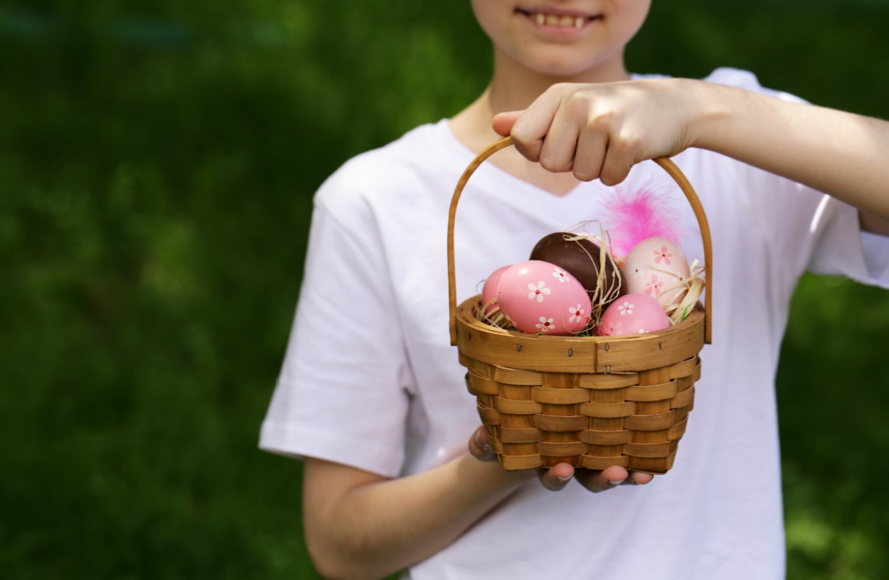 A teeange boy holding a basket full of easter eggs.