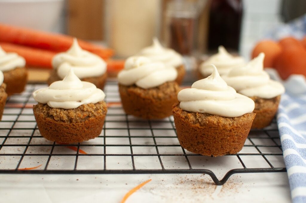 Grain-free carrot cake cupcakes with cream cheese frosting on a cooling rack.