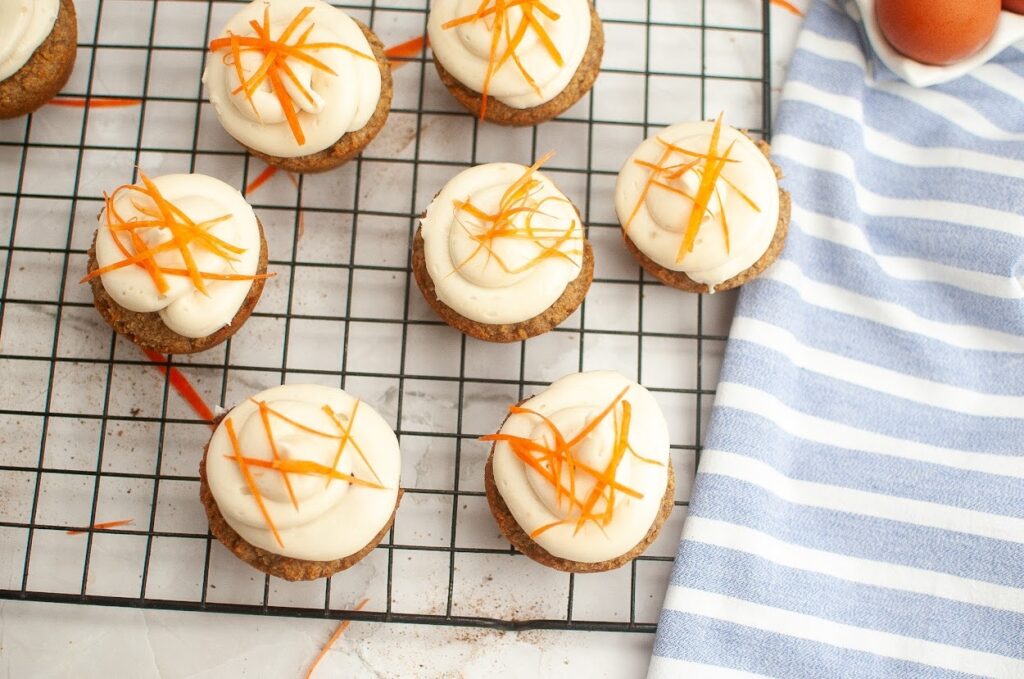 Grain-free carrot cake cupcakes on a cooling rack next to a striped towel.