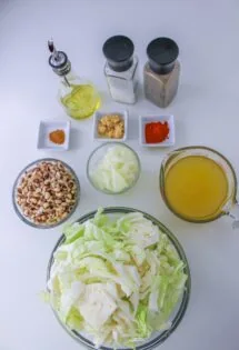 Ingredients for a recipe laid out on a table, including chopped cabbage, onions, spices, oil, and broth.