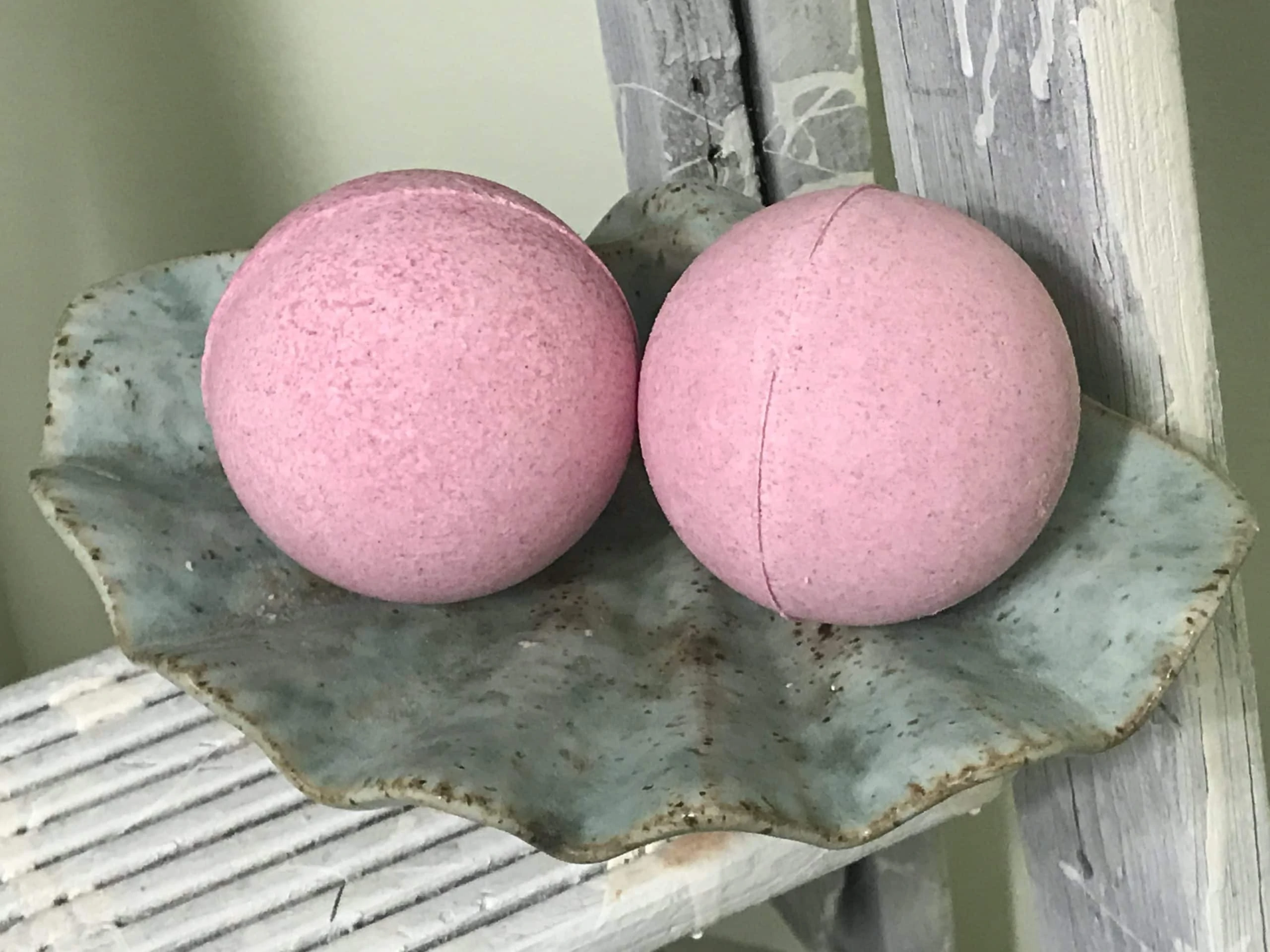2 pink DIY natural bath bombs sitting on a green soap dish shaped like a shell 