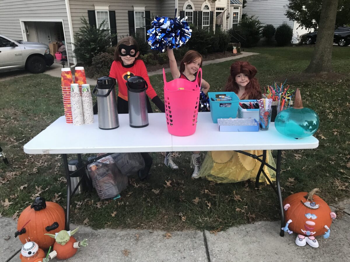 3 little girls manning a Halloween table of treats and hot apple cider
