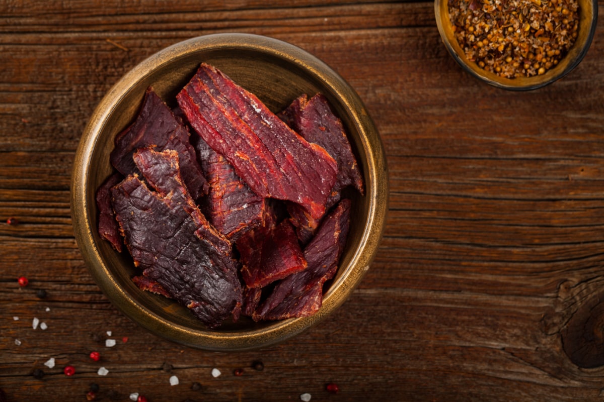 A mouthwatering display of beef jerky in a rustic wooden bowl, perfect for men's subscription boxes.