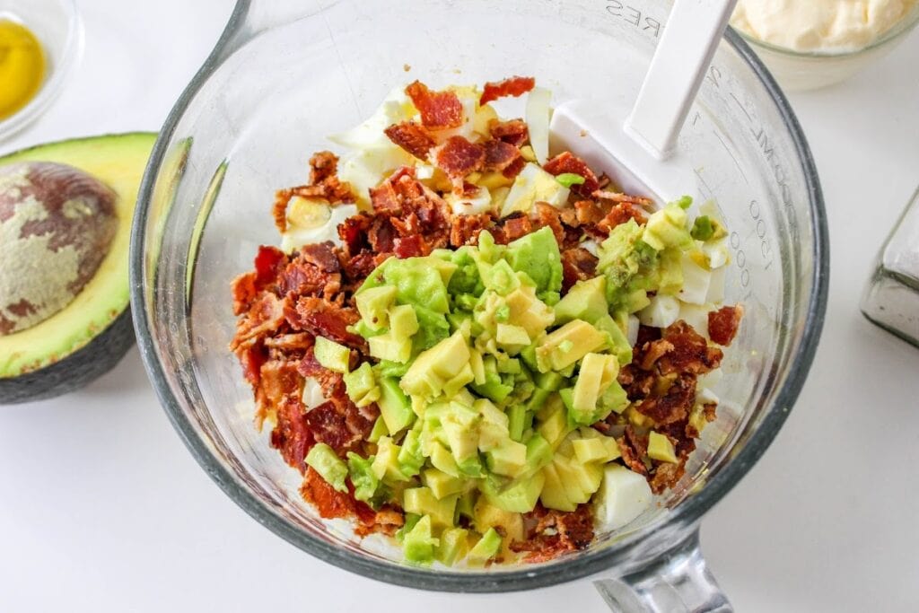 Diced avocado and crumbled bacon in a blender, ingredients for a recipe preparation.