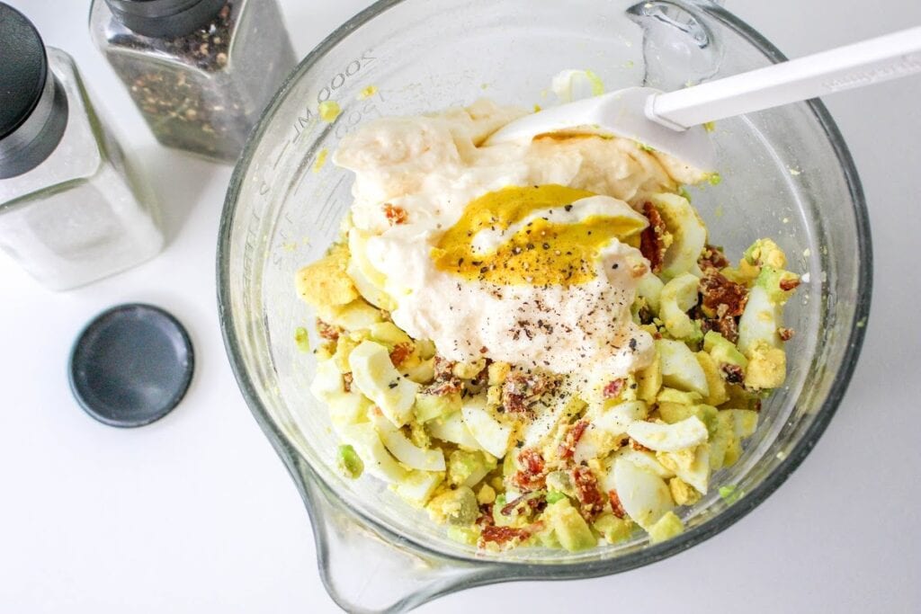 Potato salad preparation with mayonnaise, egg, and spices in a glass bowl.