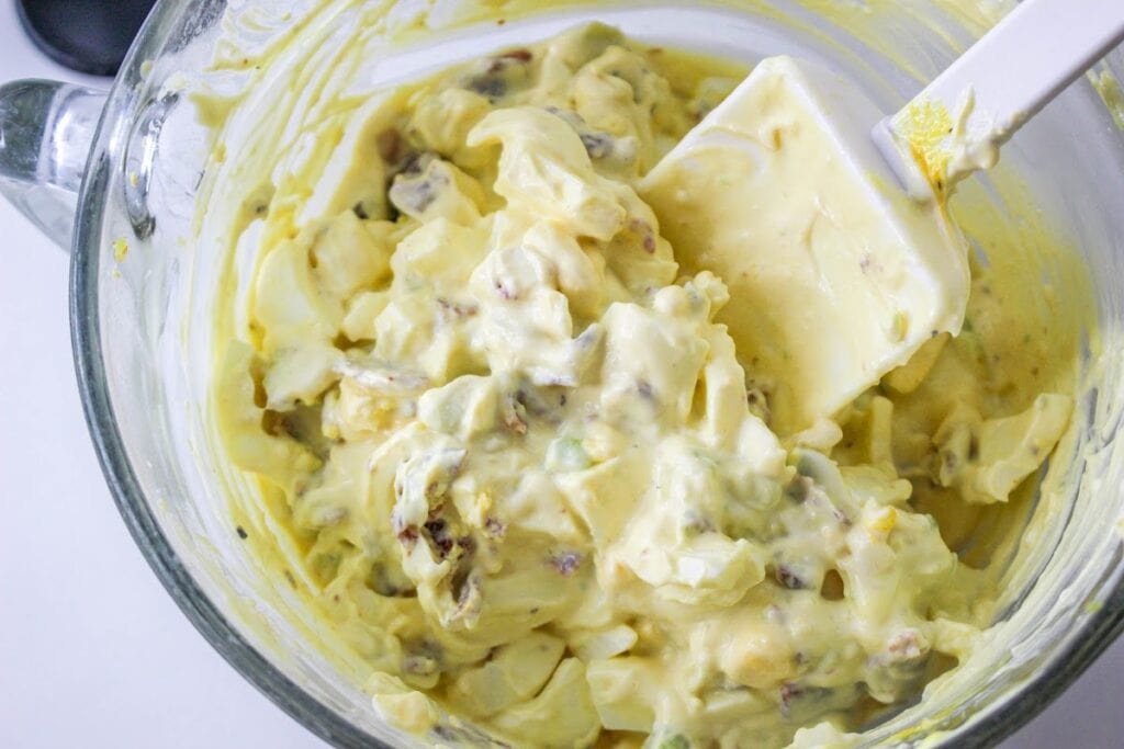 A bowl of freshly made potato salad with a mixing spoon.