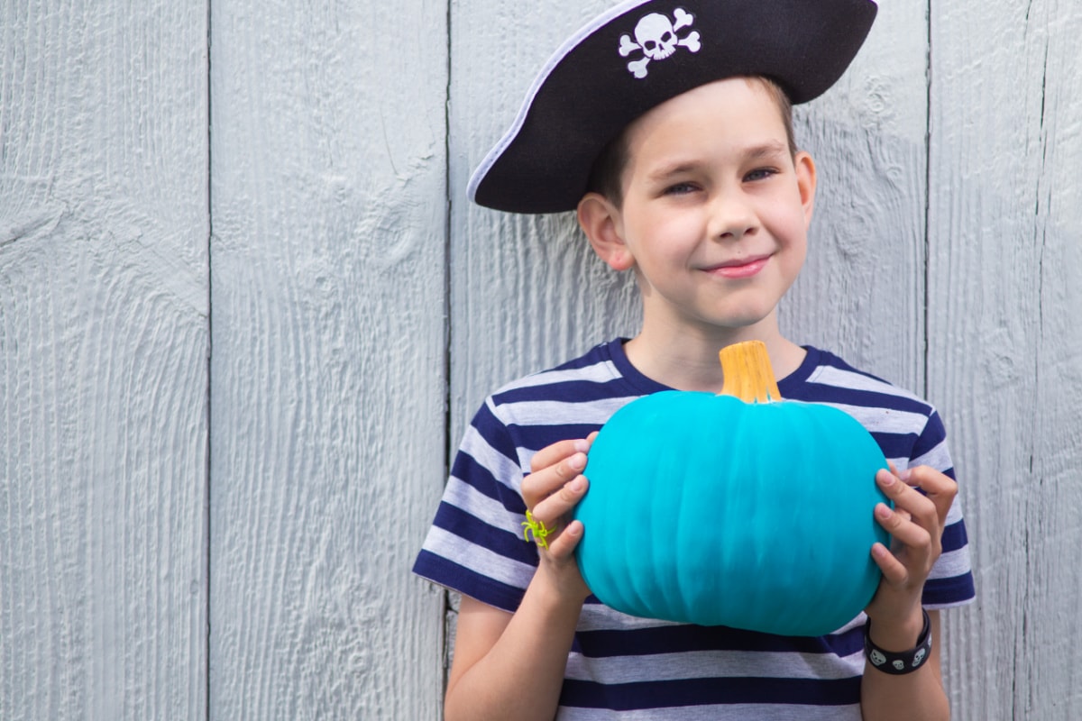 A boy in a pirate hat holding a blue pumpkin filled with non-food Halloween treats for a post on candy alternatives for Halloween.