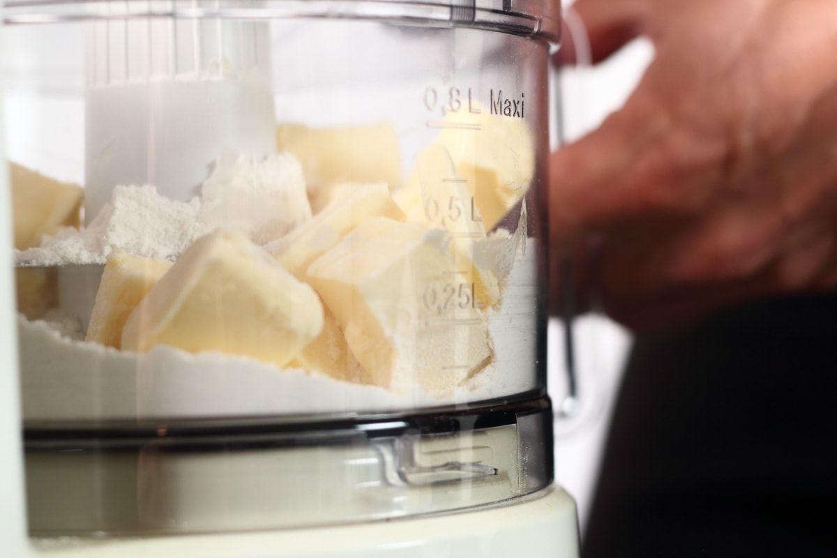 A person is putting butter into a food processor.