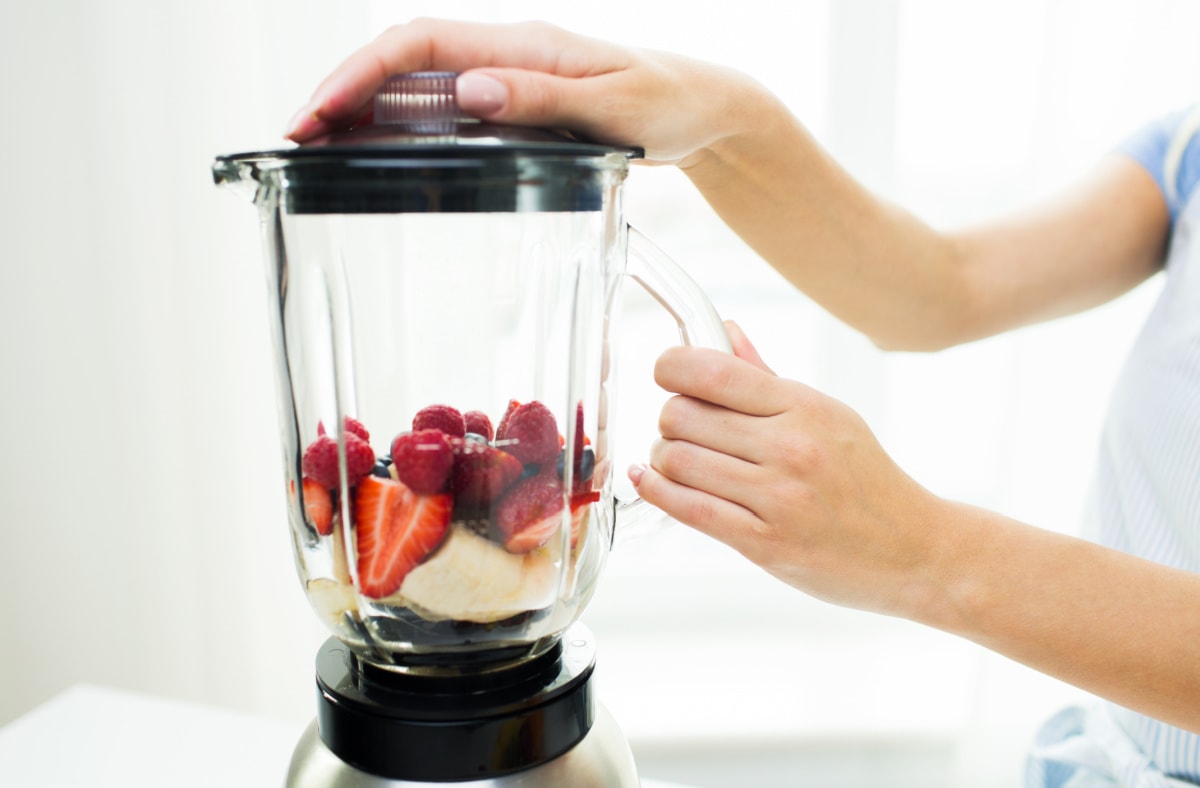 A woman is putting fruit into a blender.