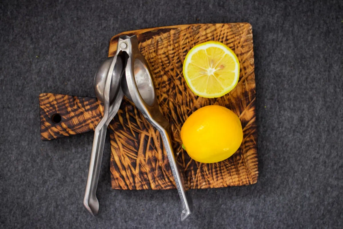 Two lemons on a wooden cutting board beside a metal lemon squeezer
