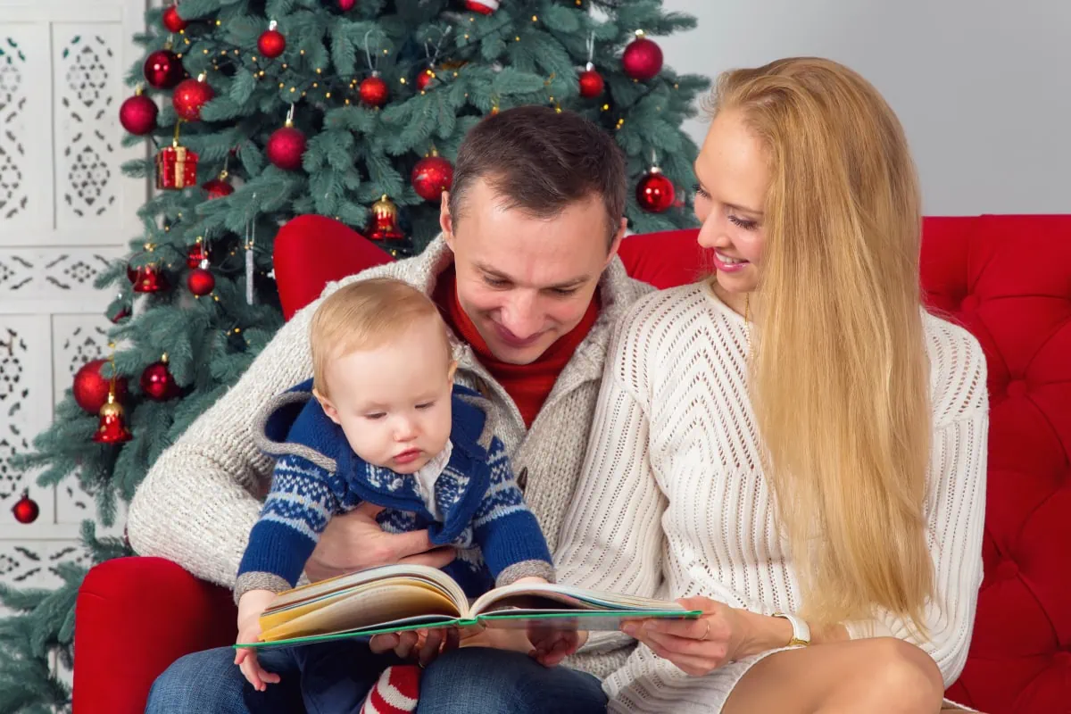 A couple reading a spiritual book to their baby in front of a Christmas tree.