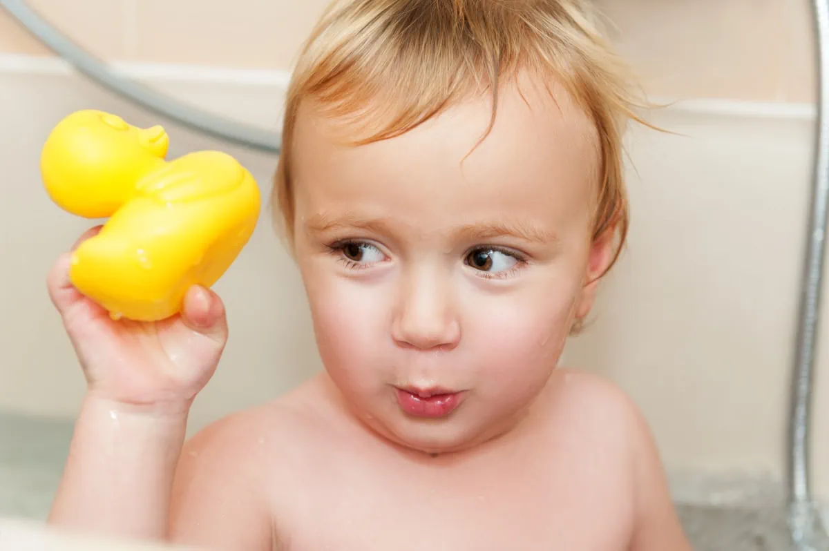 A baby holding a yellow rubber duck in a non-toy gift idea bathtub.