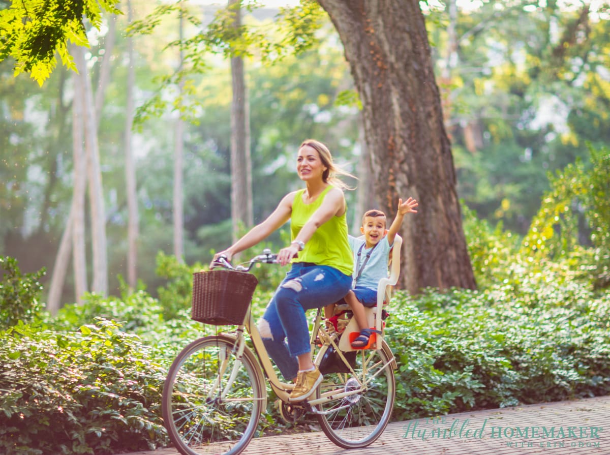 A woman and child enjoying a staycation by riding a bicycle in a park.