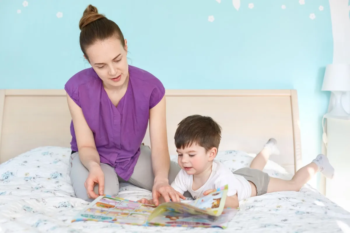 A woman sharing a non-toy gift idea with her son as they read together on the bed.