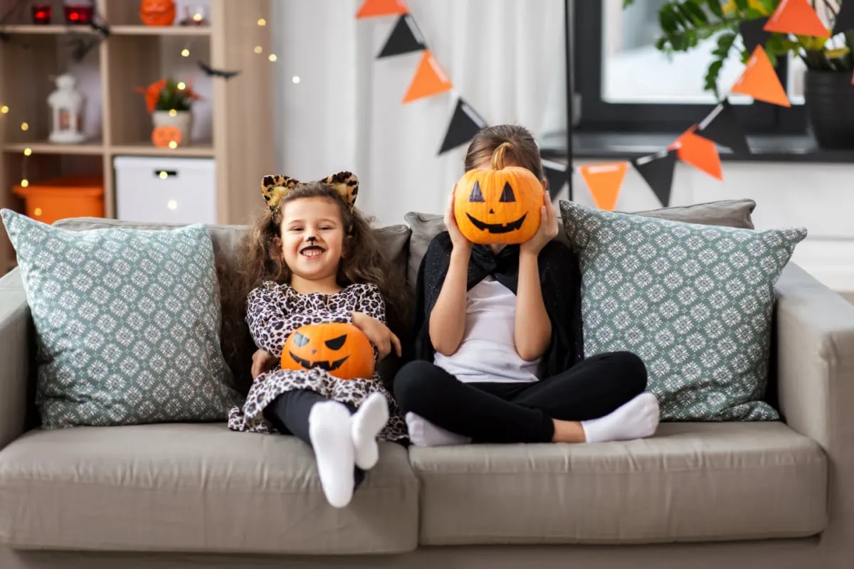 Two little girls sitting on a couch holding pumpkins, celebrating Halloween with non-food treats for a post on candy alternatives for Halloween.