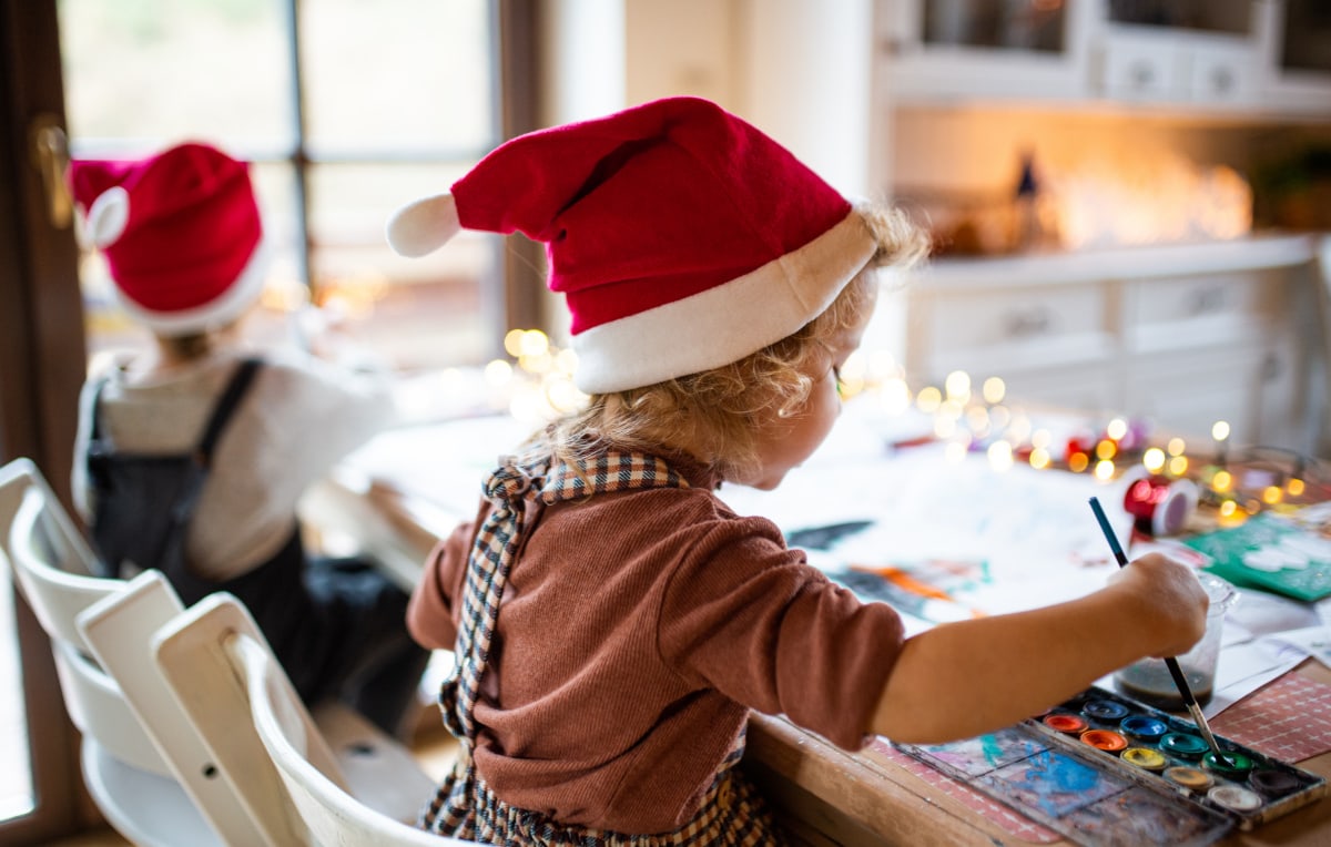 Two children wearing santa hats at a table, exchanging non-toy gift ideas.