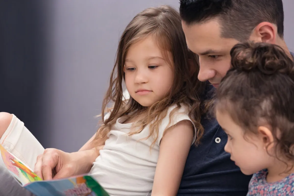 A man is sharing spiritual gift ideas with two little girls while reading a book.
