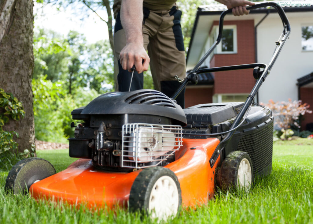 A person mowing the lawn with an orange lawnmower in a sunny backyard