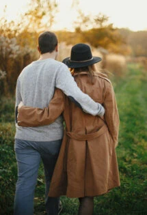 A couple embracing each other while walking through a field at sunset.