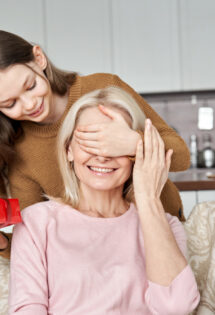 A young woman surprises an older woman with a Mothers' Day gift, playfully covering her eyes.