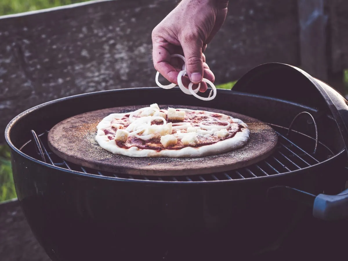 A person is preparing a pizza on a grill.