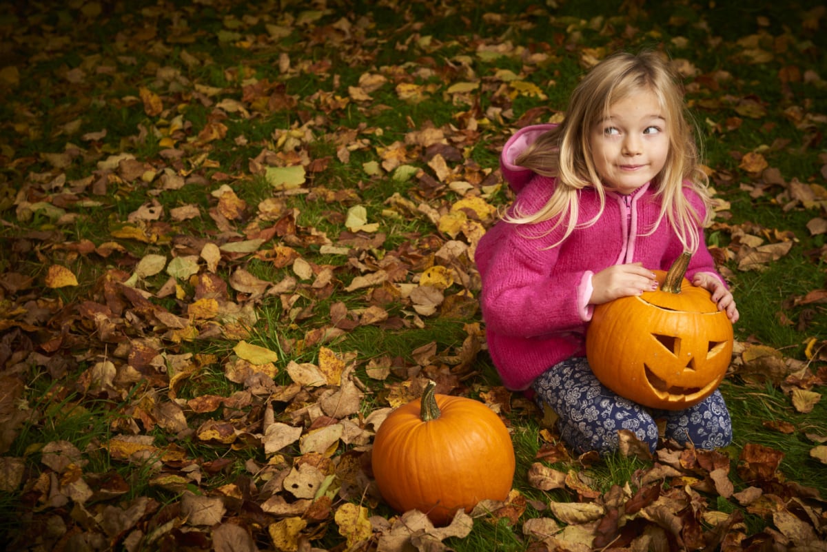 A little girl sitting on the ground with a non-food Halloween treat for a post on candy alternatives for Halloween.