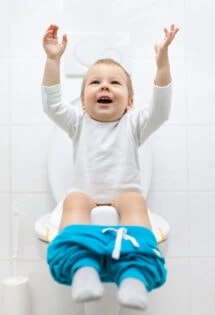 Toddler on a toilet training seat with arms raised in excitement.