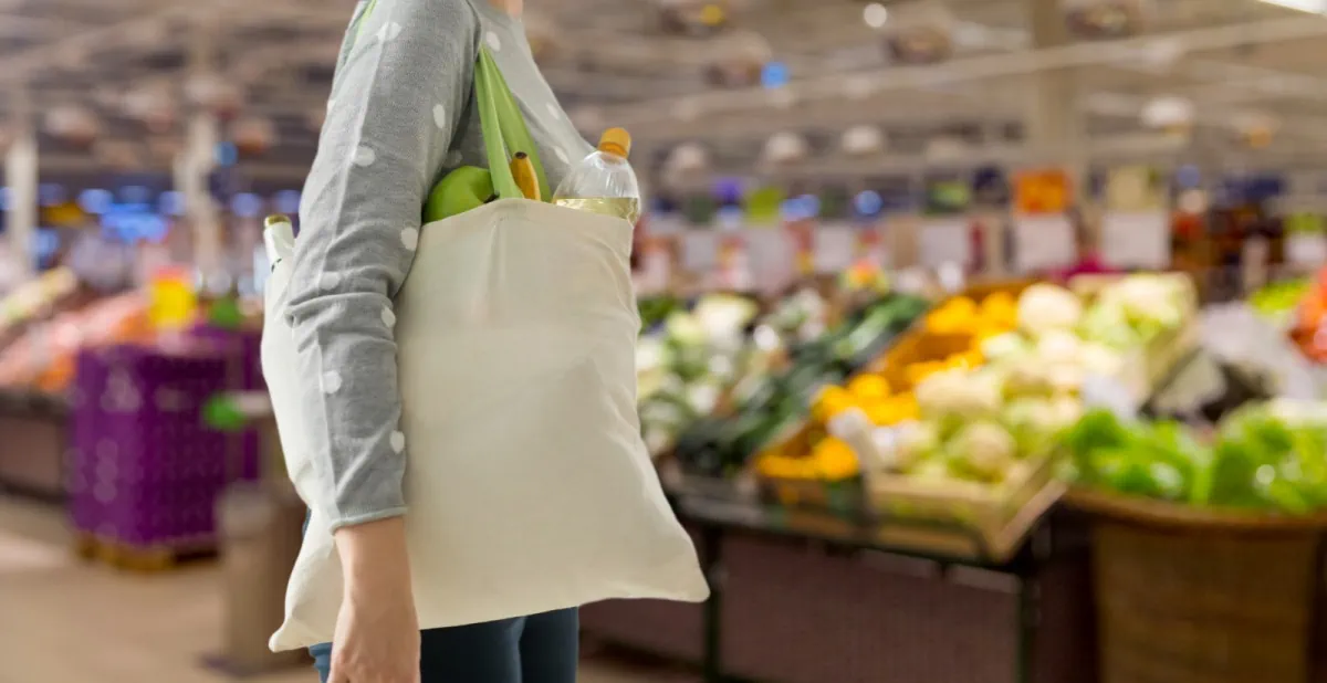 A woman is holding a tote bag during her monthly grocery trip.
