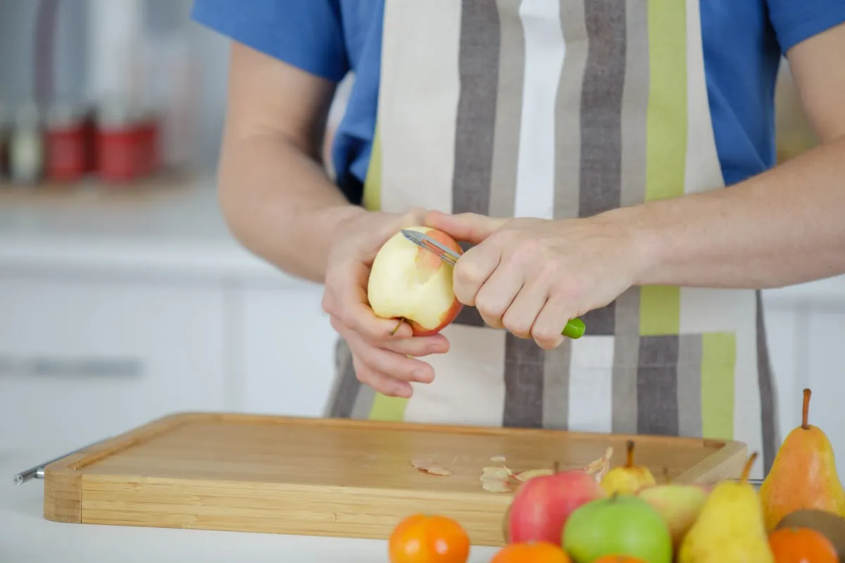 A man practicing zero waste cooking by cutting an apple on a cutting board.