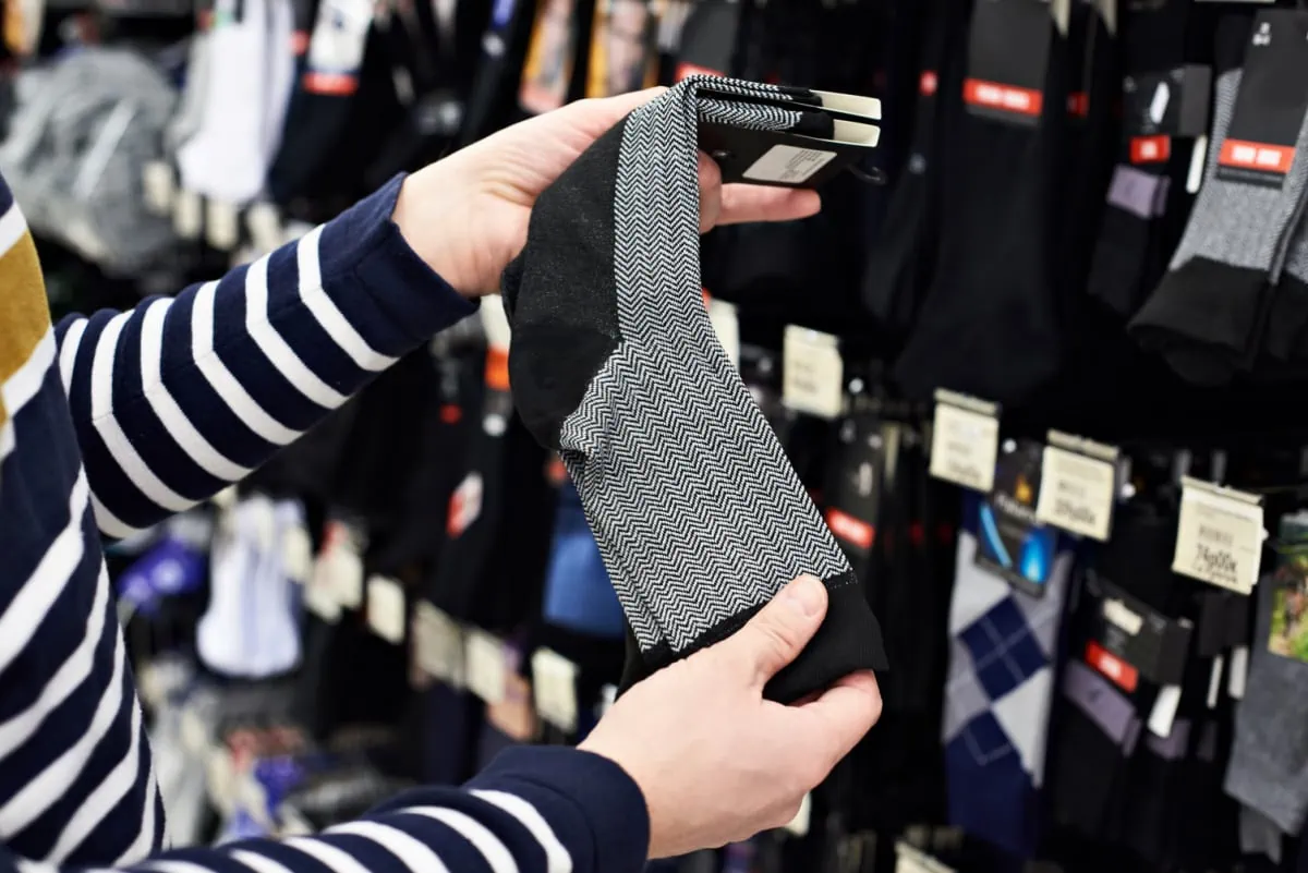 A man is examining a pair of quality socks in a store to purchase for homeless shelters since socks are the most requested item at homeless shelters.