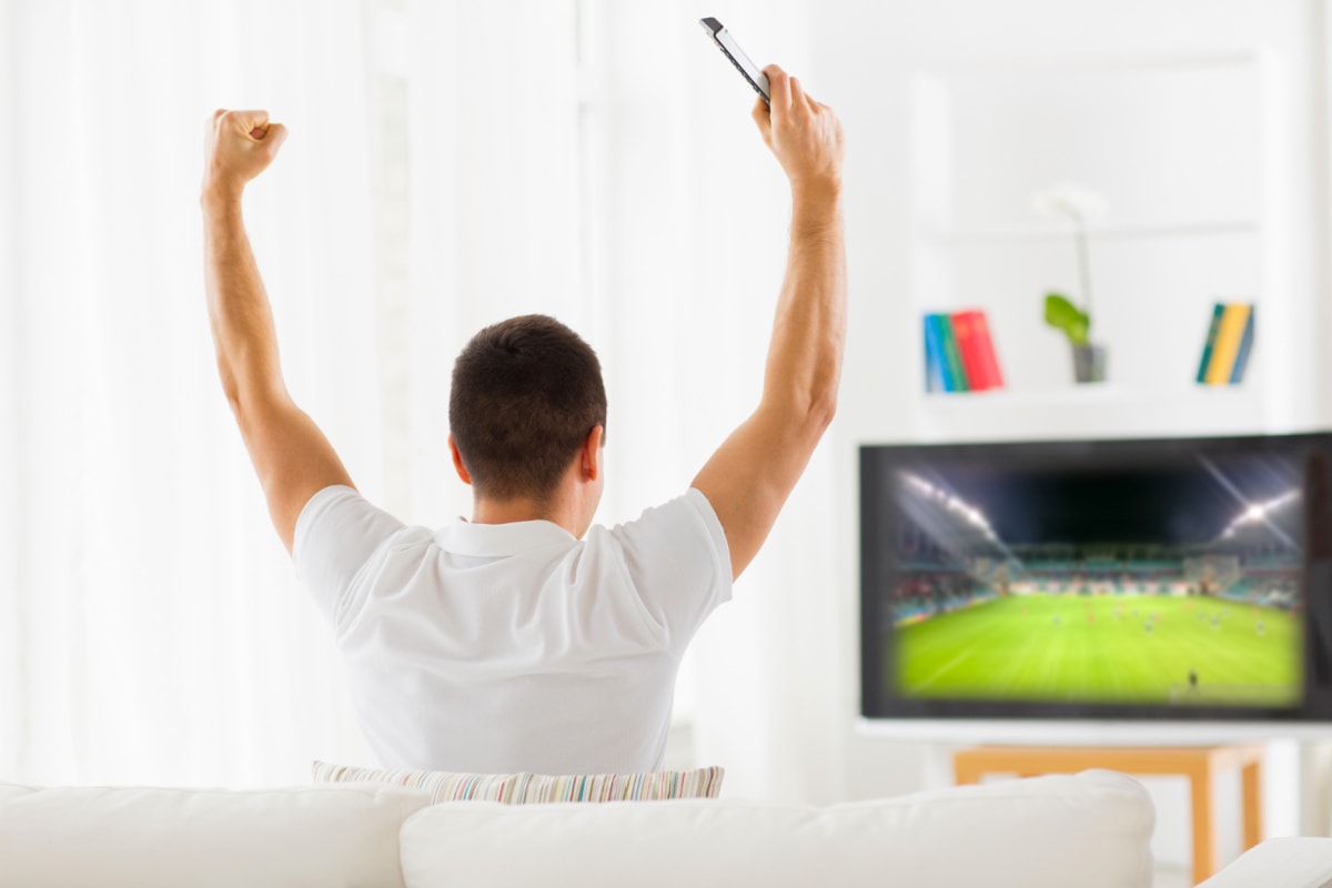 A man is sitting on a couch enjoying a football game on TV while receiving his subscription boxes for men.